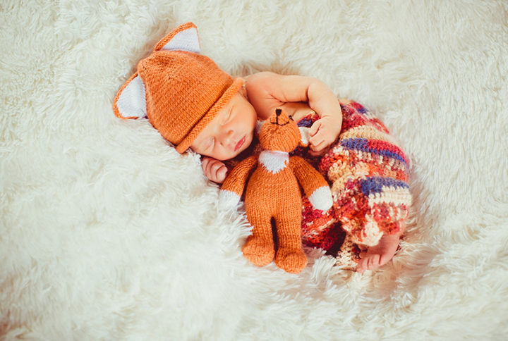 baby holds little fox toy sleeping white pillow